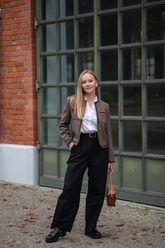 a lady in a white ruffle collared shirt, a brown jacket and a pair of black pants